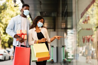 Alışveriş torbalarıyla yürüyen maskeli siyah bir çift.