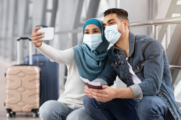 Joven pareja musulmana con máscaras médicas tomando selfie en el teléfono inteligente en el aeropuerto —  Fotos de Stock