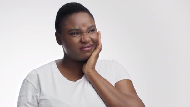 Стоматологическая боль. Студийный портрет молодой расстроенной африканской женщины, страдающей зубной болью, трогающей свою болезненную щеку — стоковое видео