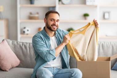Tatmin olmuş erkek müşteri karton kutudan yeni bir kazak çıkarıyor, evdeki teslimat servisinden memnun.