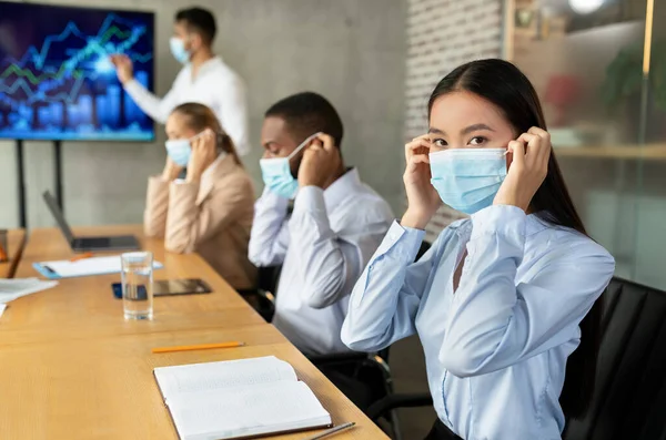 Gente de negocios multiétnicos poniendo máscaras médicas en reunión corporativa en la oficina moderna — Foto de Stock