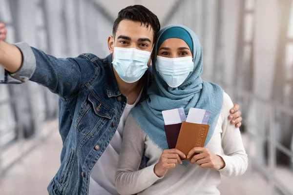 Cónyuges islámicos felices en máscaras protectoras de la cara médica tomando selfie en aeropuerto —  Fotos de Stock