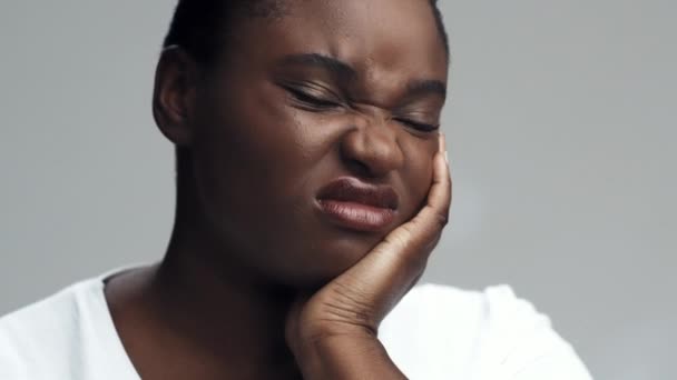 Mulher afro-americana infeliz que sofre de dor aguda de dente, tocando sua bochecha e sorridente, close up retrato — Vídeo de Stock