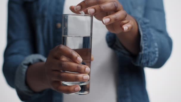 Tıbbi tedavi. Tanımlanamayan siyah bir kadının, büyük beyaz çözünür aspirin haplarını suyla bardağa koyduğu yakın çekim. — Stok video