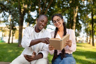Uluslararası öğrenci arkadaşlar üniversite kampüsünde dinleniyor, kitaplarla çalışıyor ve açık havada sınıfları tartışıyorlar.