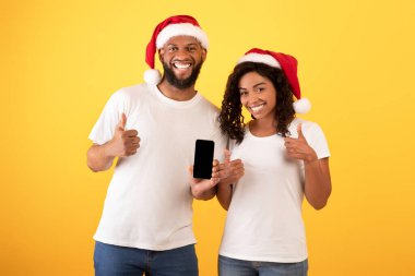 Yeni web sitesi. Beyaz ekran ile akıllı telefon tutan mutlu siyah eşler başparmaklarını kaldırıyor, sarı arkaplan