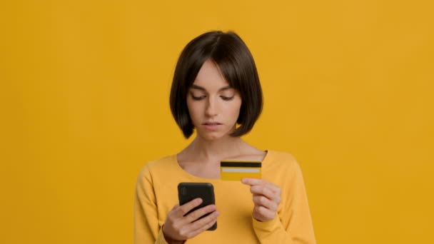 Молодая леди с помощью смартфона и кредитных карт покупки, желтый фон — стоковое видео