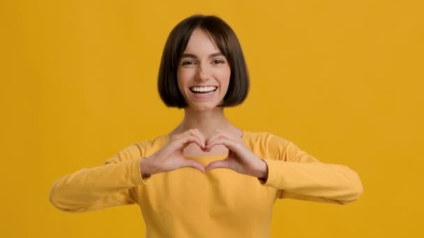 Nő Gesturing szív alakja ujjakkal mutatja szívverés, sárga háttér — Stock videók