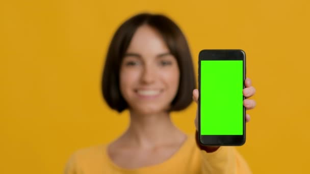 Mujer mostrando Smartphone con pantalla de clave de croma vacío, fondo amarillo — Vídeo de stock