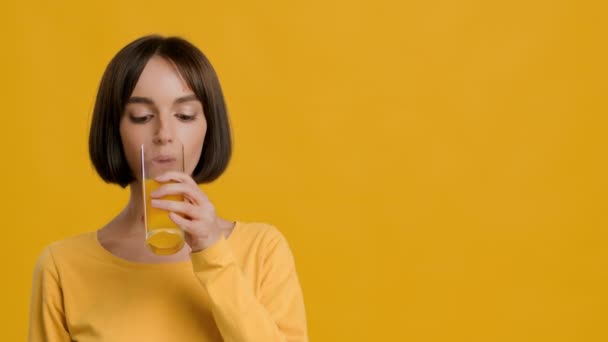 Wesoła kobieta Picie szklanki soku pomarańczowego na żółtym tle — Wideo stockowe