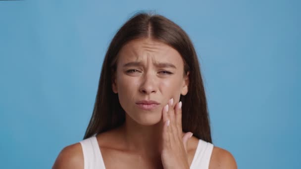 Mulher infeliz sofrendo de dor de dente tocando bochecha sobre fundo azul — Vídeo de Stock