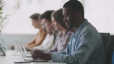 Modern teknoloji ve eğitim. Genç Afrikalı Amerikalı öğrenci dizüstü bilgisayarla yazı yazıyor, grup arkadaşlarıyla oturuyor.