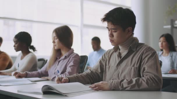 Diverse junge College-Studenten schreiben während des Unterrichts Notizen oder Prüfungen, sitzen im Klassenzimmer und schauen auf die Tafel — Stockvideo