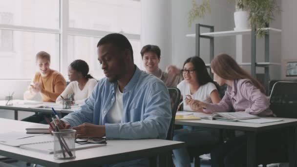 Ung afrikansk amerikan som lider av gruppkamrater, sitter isär i klassrummet, elever kastar pappersbollar på honom — Stockvideo