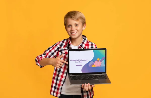 Улыбающийся кавказский мальчик, указывающий на экран ноутбука с веб-сайтом школы для детей, оранжевый фон — стоковое фото