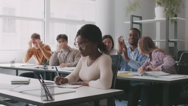 Victim of bullying. African american girl sitting alone in classroom, rude groupmates laughing at her — Stock Video