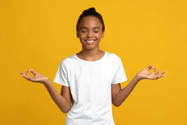 Smiling peaceful cute teen afro american lady pupil in white t-shirt with closed eyes meditation — Stockfoto