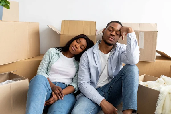 Real estate and renting issues concept. Sleepy african american couple sitting among cardboard boxes, being tired