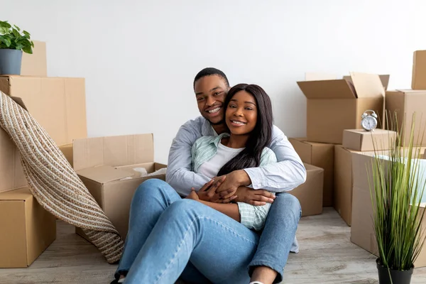 Retrato de cônjuges afro-americanos amorosos abraçando entre caixas de papelão depois de se mudar para o próprio apartamento — Fotografia de Stock