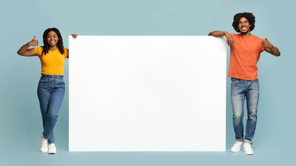 Feliz pareja afro-americana de pie junto a tablero horizontal vacío para publicidad —  Fotos de Stock