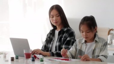 Koreli Anne, kız içeride resim yaparken bilgisayarda çalışıyor.