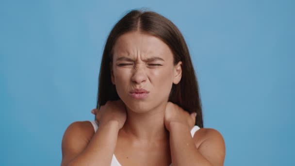 Woman Suffering From Nechache Massaging Aching Neck On Blue Background — Stockvideo