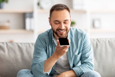 Neşeli milenyum çocuğu evinde cep telefonuyla koltukta oturuyor, cep telefonu uygulaması ya da ekranda web sitesi için modelleme yapıyor.