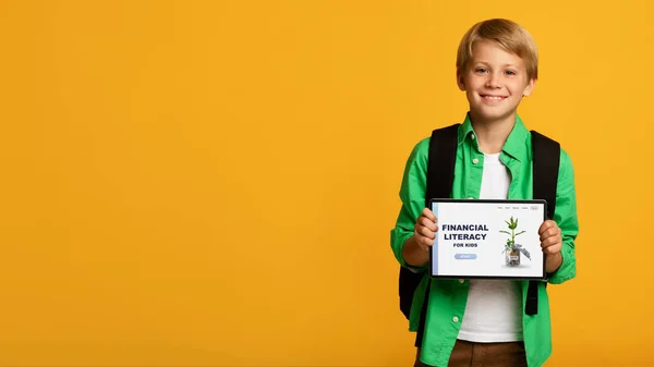 Alegre chico demostrando tableta ordenador con Educación Financiera Para Niños sitio web de la escuela en línea en fondo naranja — Foto de Stock