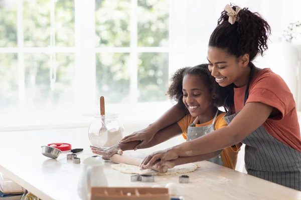 Весела чорна мати допомагає доньці розкачувати тісто пасті — стокове фото