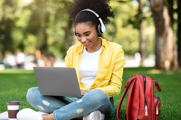 Africano studente ragazza apprendimento su computer portatile indossando auricolari in parco — Foto Stock