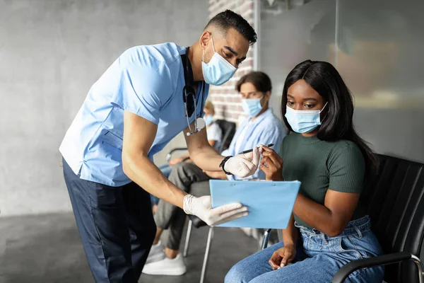 Señora negra con mascarilla firmando expediente médico antes de la vacunación —  Fotos de Stock