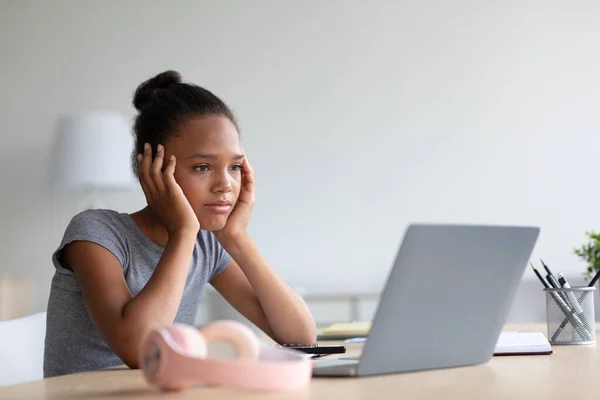 Triste cansado aburrido bastante adolescente afroamericano niña alumna en los auriculares estudio en casa con el ordenador portátil — Foto de Stock