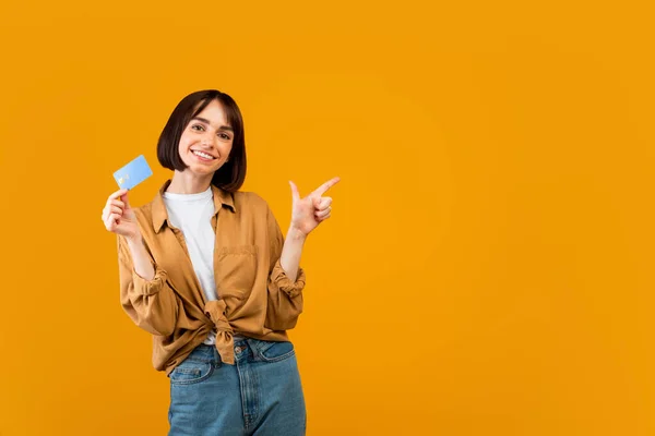 Eccitato signora con carta di credito indicando da parte lo spazio vuoto su sfondo studio giallo, panorama — Foto Stock