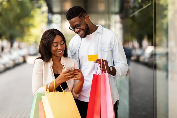 Portrait of happy afro couple using smartphone holding credit card — Stock Photo, Image