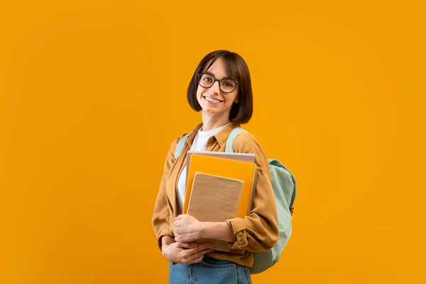 Academisch onderwijs. Jongedame met rugzak en notitieboekjes glimlachend op camera over gele studio achtergrond — Stockfoto