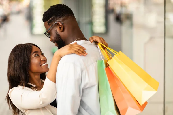 Gelukkig zwart paar knuffelen en houden boodschappentassen — Stockfoto