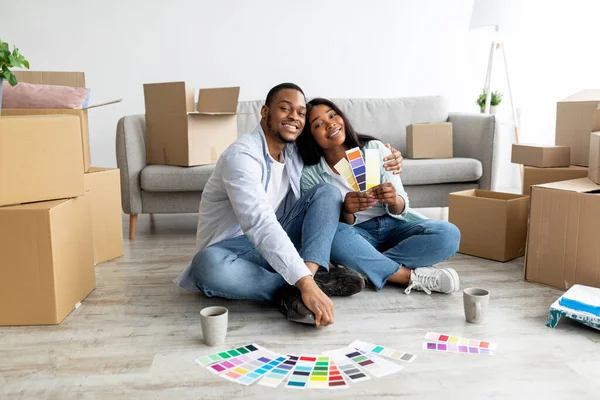 Feliz pareja afroamericana planeando renovación y soñando, eligiendo paletas de colores juntos, sentados en una casa nueva — Foto de Stock