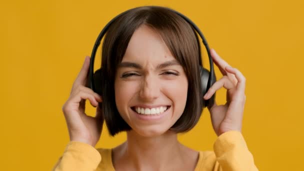 Mulher milenar positiva usando fones de ouvido ouvindo música em fundo amarelo — Vídeo de Stock