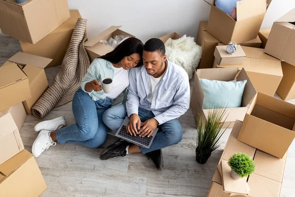 Moviéndose, reubicando el concepto. Amar pareja afroamericana comprar muebles para un nuevo apartamento, utilizando el ordenador portátil —  Fotos de Stock