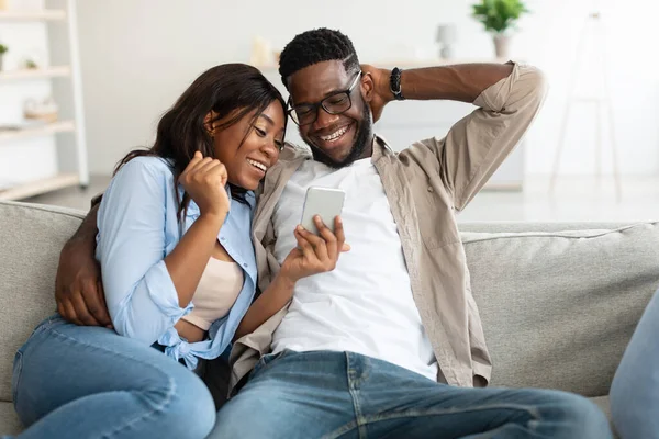 Africký americký pár sedí na gauči, pomocí mobilu — Stock fotografie
