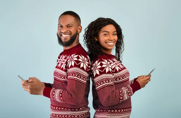 Nyårs- och julkampanjer. Glad afrikansk amerikansk man och kvinna håller smartphones och står tillbaka mot ryggen — Stockfoto