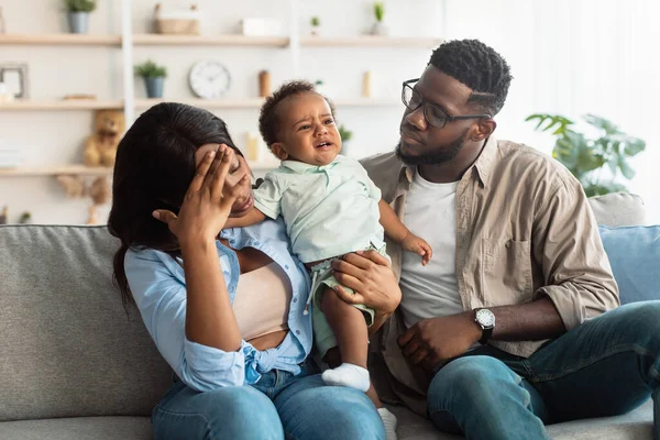 Moe zwarte ouders zitten met huilen kind op de bank — Stockfoto