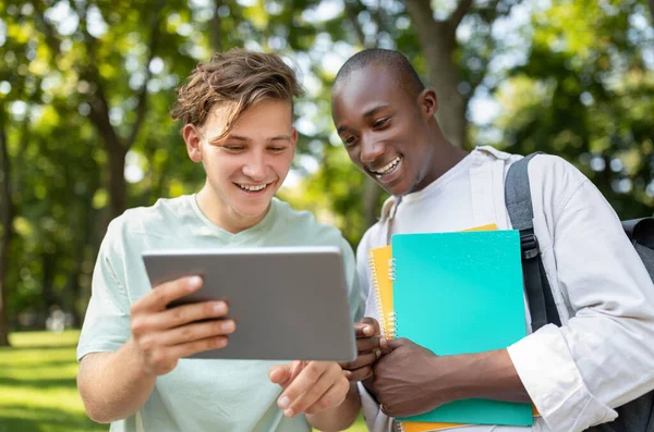 Estudiante mostrando su proyecto en tableta digital a un amigo, caminando al aire libre en el campus universitario —  Fotos de Stock