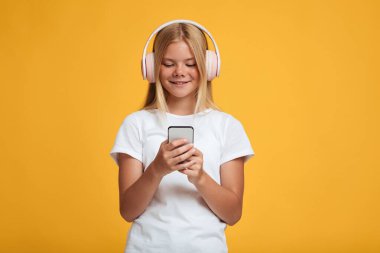 Beyaz tişörtlü, kablosuz kulaklıklı gülümseyen Avrupalı genç bayan müzik dinler, video izlerdi.