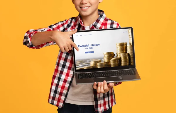 Close-up van gelukkige jongen wijzen naar laptop scherm met financiële geletterdheid voor kinderen educatieve website, oranje achtergrond — Stockfoto