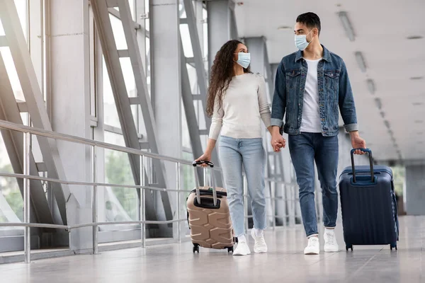 Coppia mediorientale che indossa maschere protettive per il viso camminando con valigie in aeroporto — Foto Stock