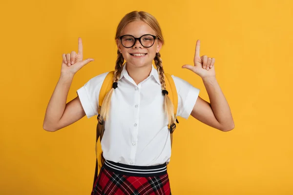 Cheerful young blonde female schoolgirl with pigtails in glasses shows thumbs up at free space — Stock Photo, Image