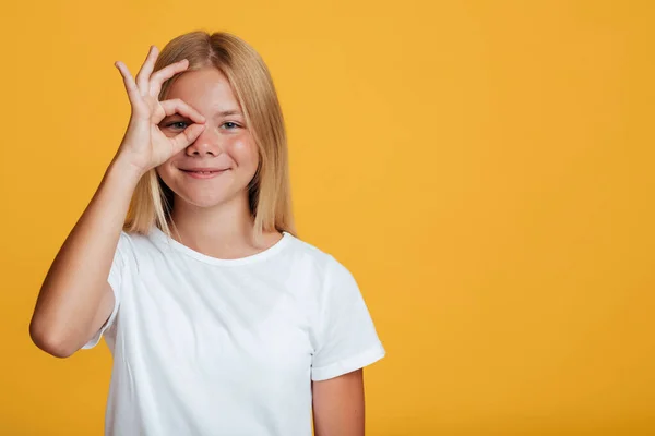 Щасливий красивий підліток блондинка леді зіниця в білій футболці показує ок жест біля очей — стокове фото