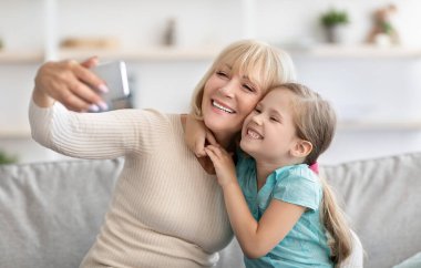 Aile selfie 'si. Ev içinde selfie çeken çok nesilli bir ailenin portresi. Küçük torunuyla poz veren mutlu büyükanne cep telefonu kullanıyor. Bağ ve Yaşam Tarzı Konsepti
