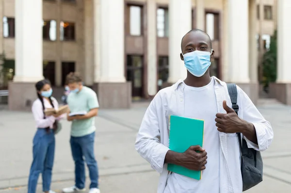 Tanulj a koronavírus alatt. Fekete férfi diák visel arc maszk, gazdaság notebook és pózol a kamera a szabadban — Stock Fotó
